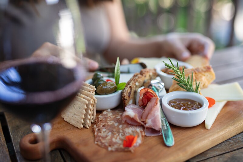 A plate of cheese, charcuterie, and pecans with a blurred glass of red wine in the foreground