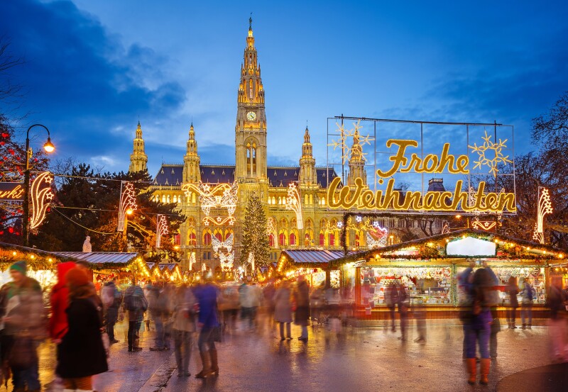 Outdoor Christmas market in Vienna at dusk, with large, lit City Hall in background