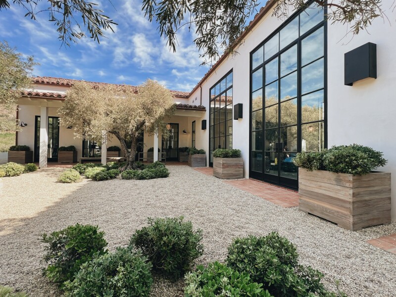 Courtyard at the Ranch Malibu shaded by trees; white one-story building with wall of windows