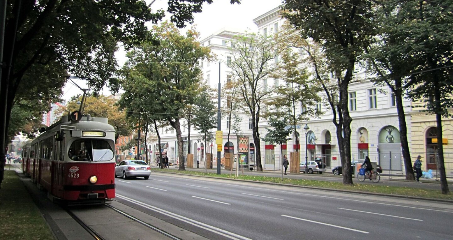 A red streetcar on a road divided by a line of trees.