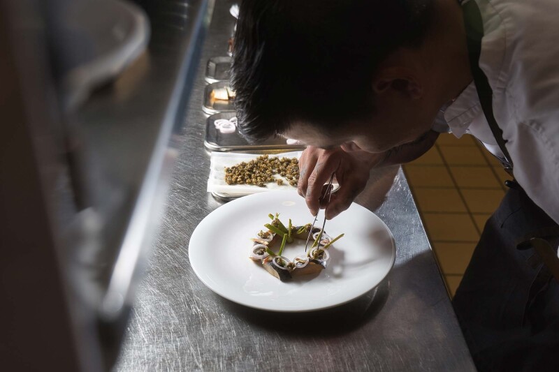A chef leaning over and using tweezers to put the final touches on a dish