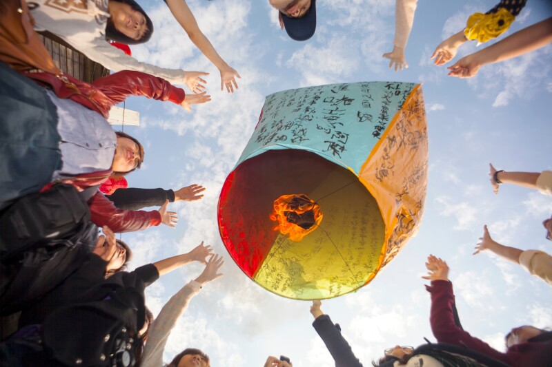 People with arms stretched up surrounding large lantern viewed from below