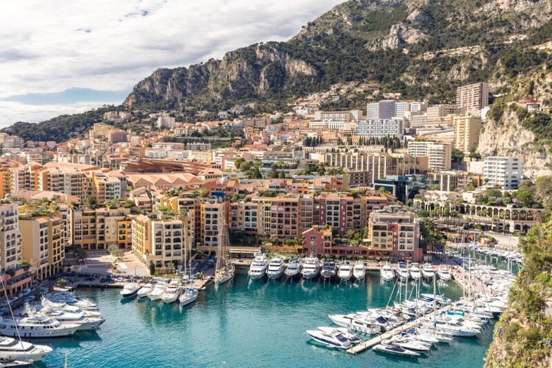 Seaside buildings crowded near a yacht dock, with hills in distance