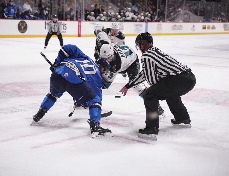 Two hockey players facing off as a referee drops a puck on the ice in a rink in South Lake Tahoe.
