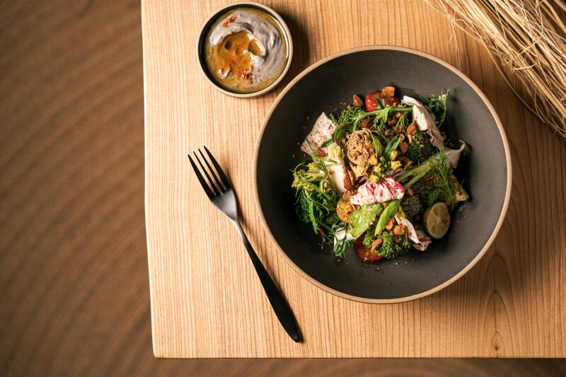 Overhead view of bowl of mixed vegetables on a blond wood table, with a fork