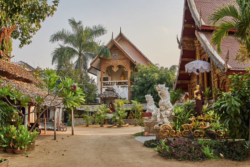 Wooden buildings among greenery, one with intricately carved animal statues in front