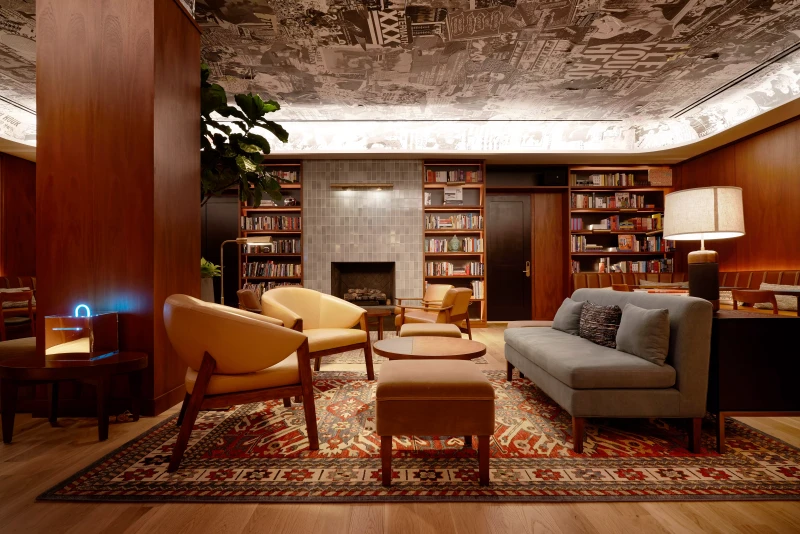A lobby space with deep-set couches, ottomans, and chairs, shelves filled with books, and a ceiling papered with black-and-white posters