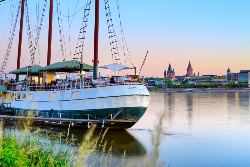 A view of people on a large sailboat looking across the Rhine river at Saint Martin's Cathedral in Mainz, Germany.
