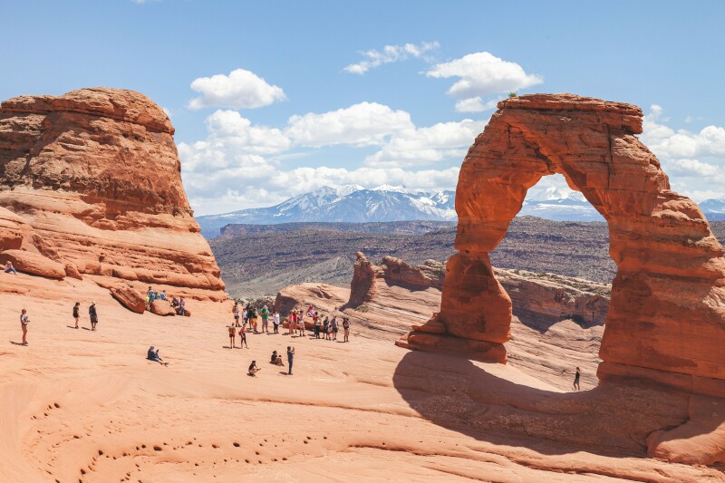 More than 10 people stand near a stone arch overlooking mountains