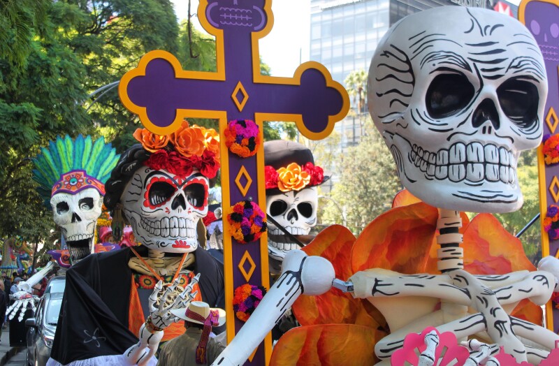 Skeletons on float with purple and orange cross during Dia de los Muertos parade in Mexico City