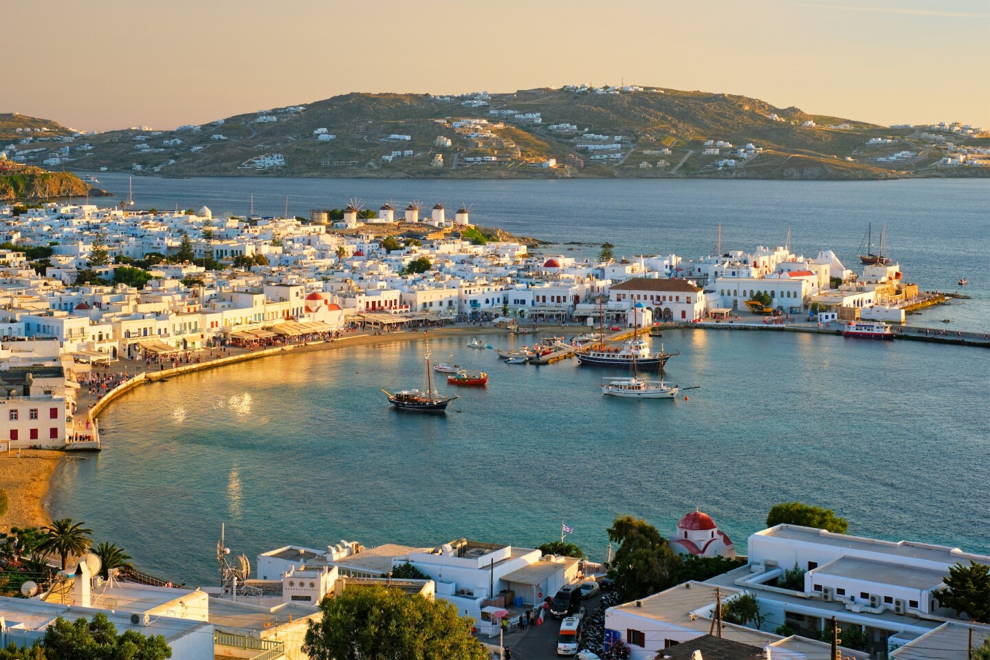 A whitewashed town around a bay with mountains in the background and boats in the water