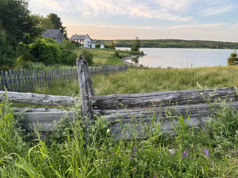 An old wooden fence, with a stretch of river and a few cottages in the distance
