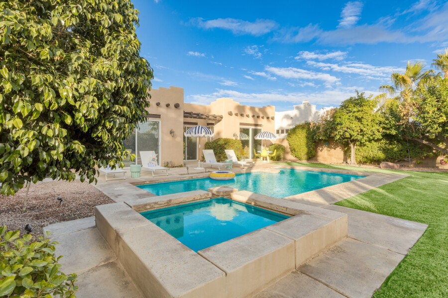 A rectangular outdoor pool with square hot tub, with adobe style building in distance
