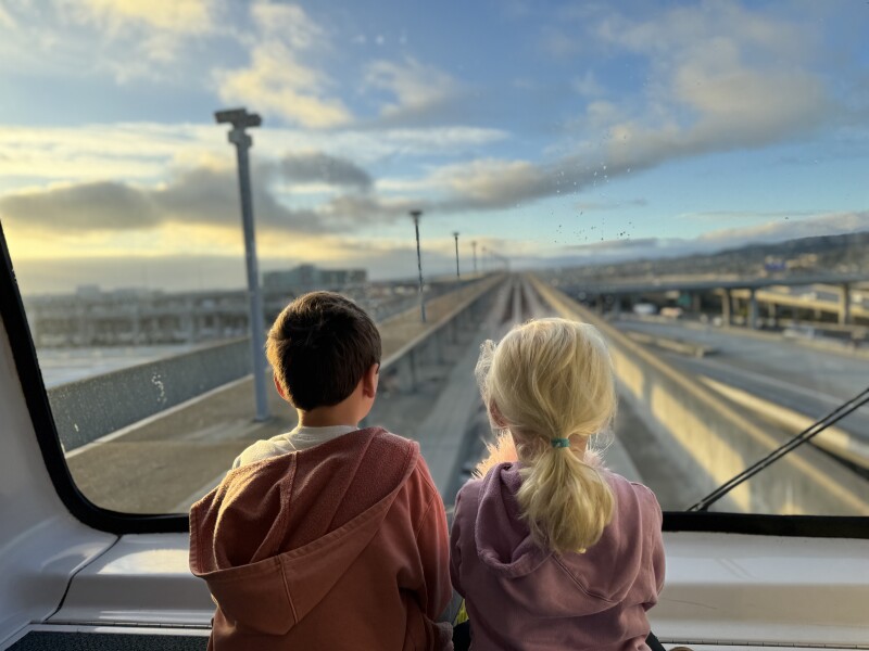 Two young children sitting at the large front window of the AirTrain at San Francisco International Airport