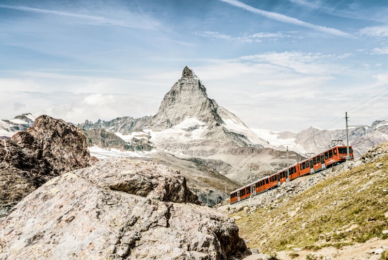red train traveling over mountainous land in Switzerland with the pointy Matterhorn mountain in the background