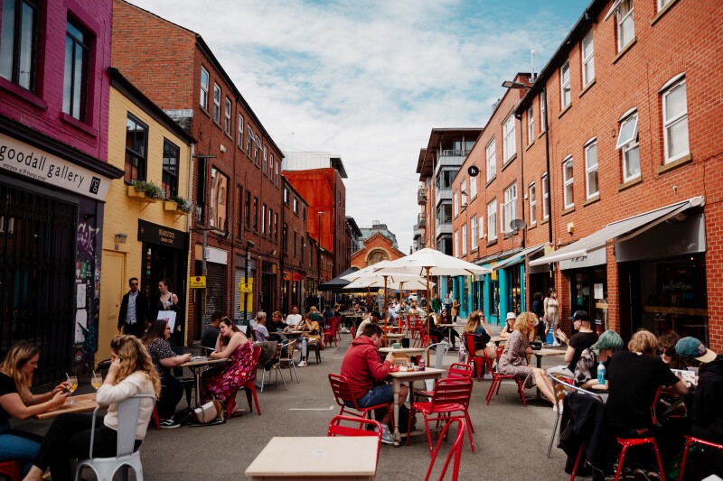 A pedestrian-only street in Manchester, with people sitting at outdoor café tables between brick buildings