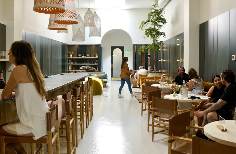 Gray and white interior of Marine Layer Wines, with one person seated at bar on left and a few people at round tables at right