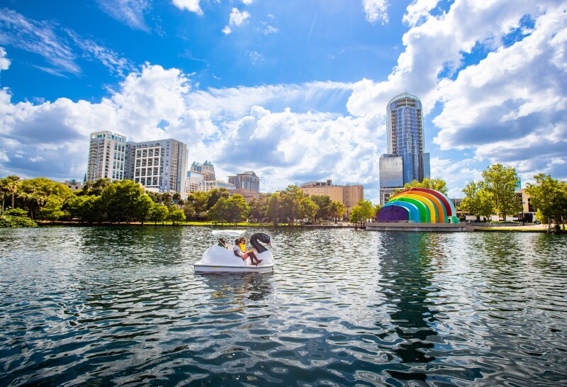 People in small swan-shaped boat on lake, with skyscrapers in background