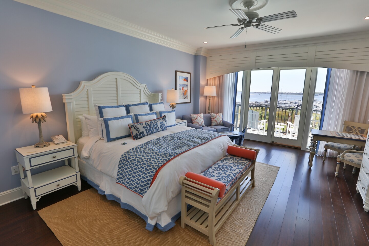 A King room at the Beach Club, with hardwood floor, ceiling fan, small balcony, and bed with a white headboard and blue and white pillows