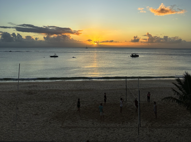 A few volleyball players on the beach during sunset, with two small boats offshore