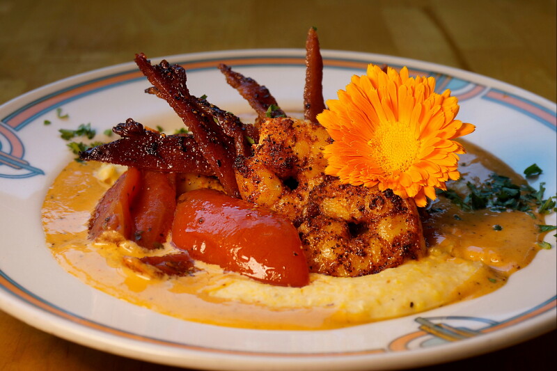 shrimp and grits on polenta served on a plate with a marigold flower