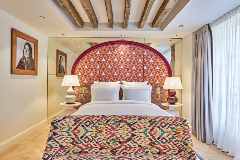 Guest room, with wood-beam ceiling, large window, and patterned headboard and seating at foot of bed
