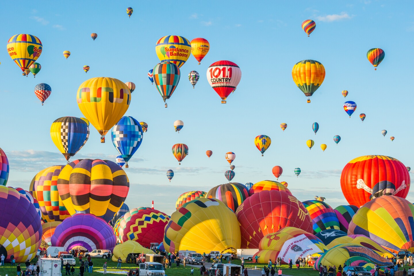 Colorful hot air balloons flying over field of balloons not fully inflated