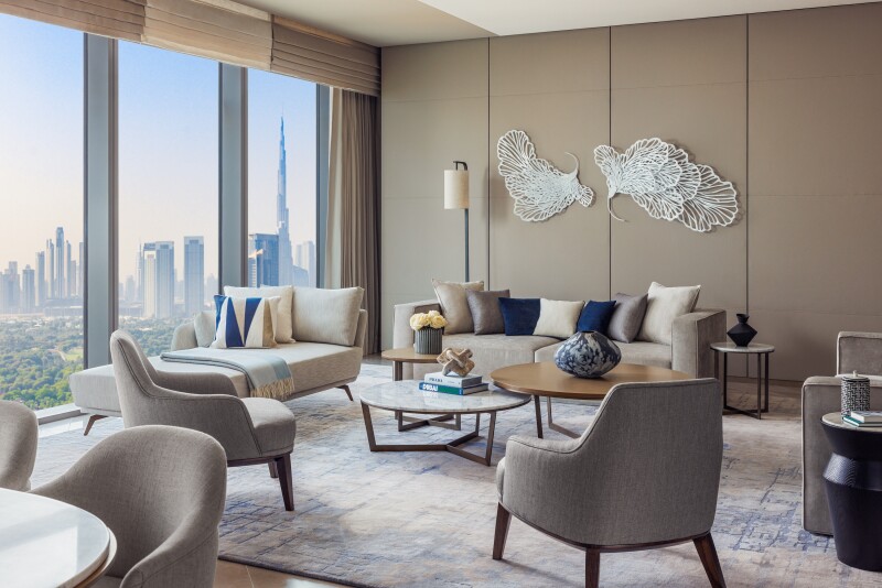 The beige living room of a Skyline Suite, with a large chaise longue and a sofa with city views from floor-to-ceiling windows
