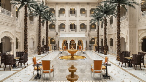 This public space at the Raffles Jaipur in Rajasthan has large palm trees and scalloped arches, with a gold fountain at its center.