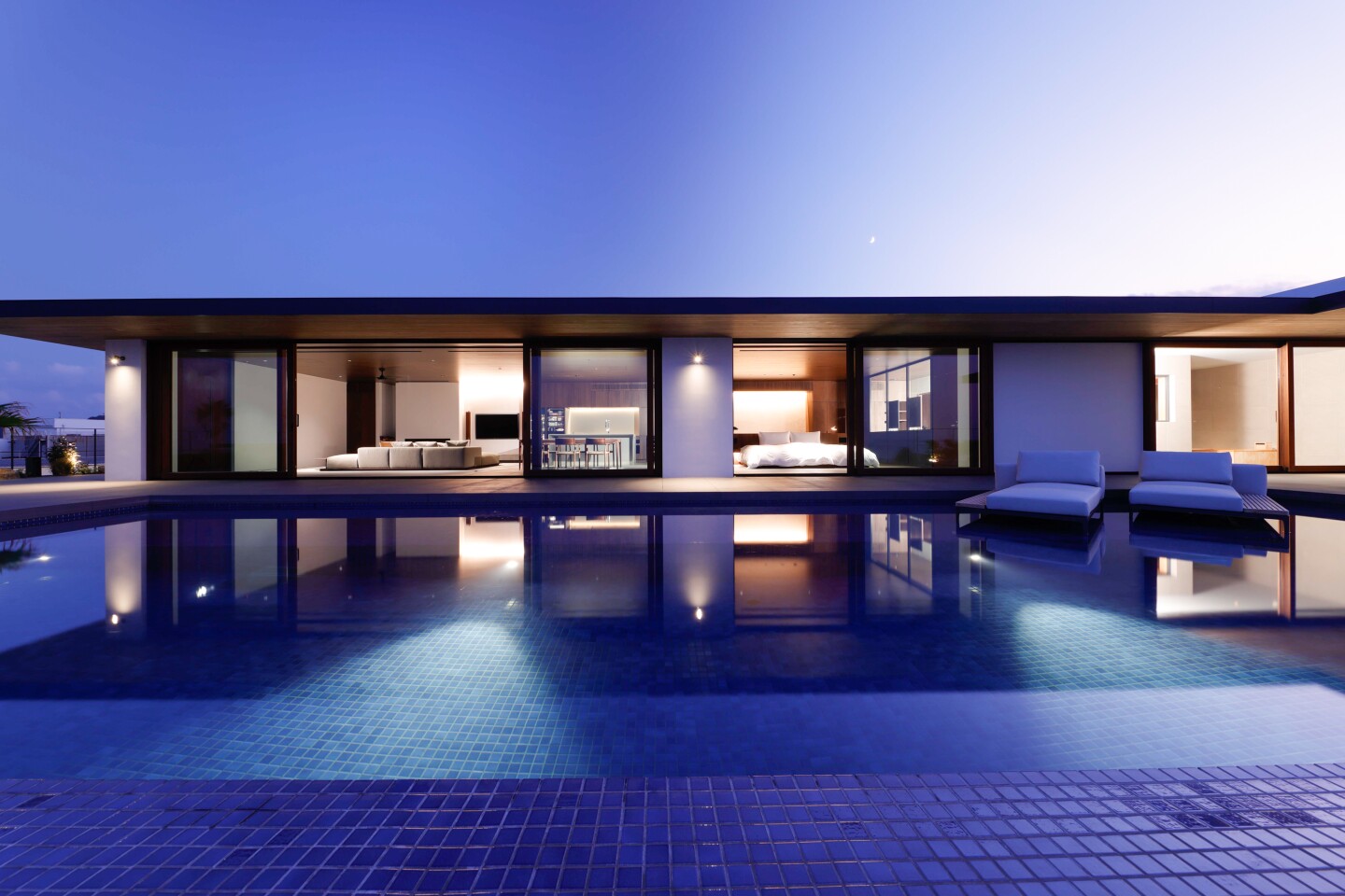 Exterior of modern one-story Not a Hotel Aoshima at dusk, reflected in pool