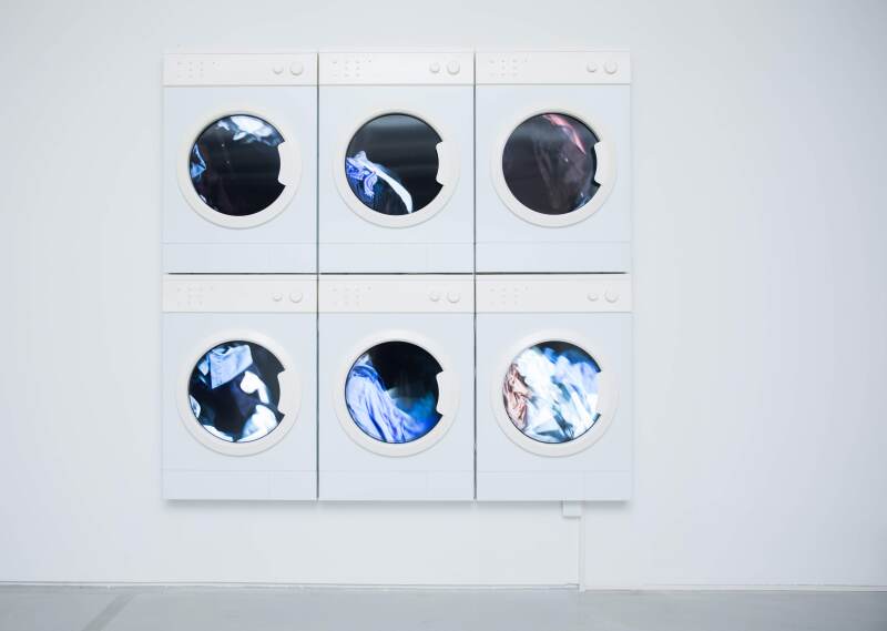 “Laundry Six Cycles,” a recent painting by Leandro Erlich, depicts six wall-mounted washing machine doors with circular windows.