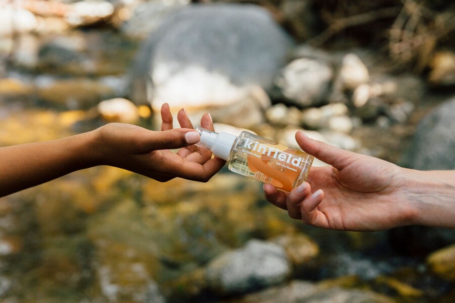 A pair of hands passing off a bottle of buy spray