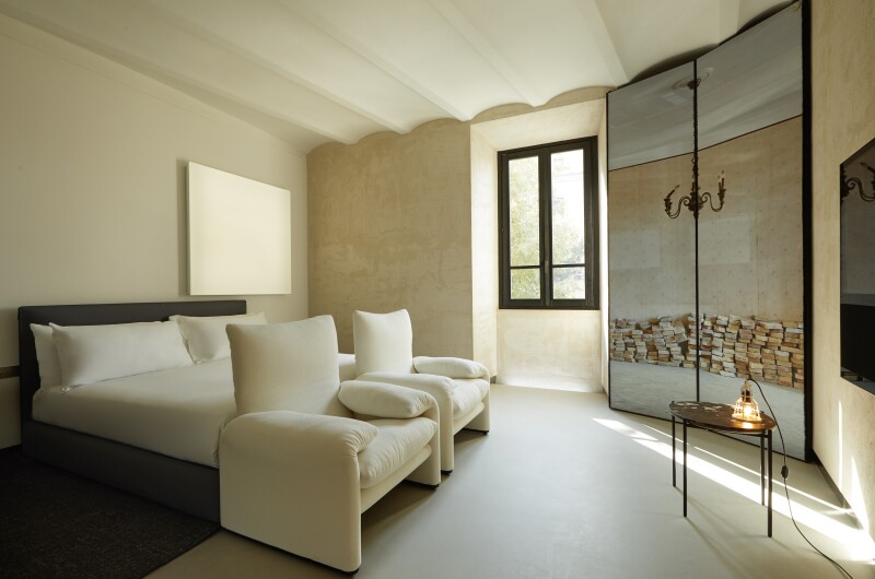 The bed, walls, and bathroom of the Rooms of Rome's rooms are all cream and beige colored. Minimalistic artwork over the bed.