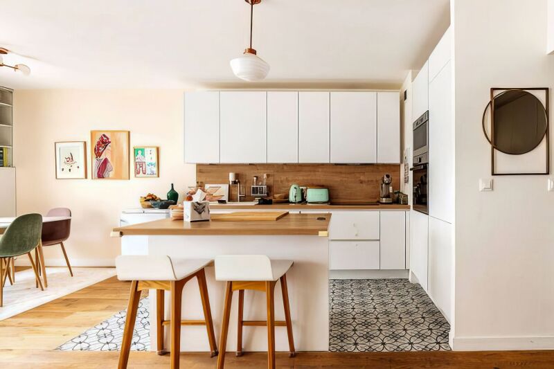 White kitchen in a HomeExchange Paris apartment, with island with wood top and two high stools