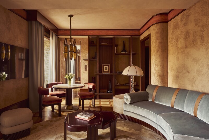 A suite's living room, with curving gray sofa and several chairs and small tables