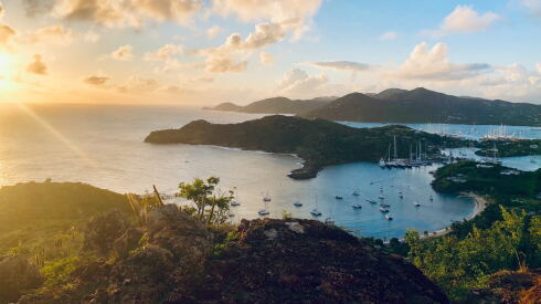Bay in Antigua with sailing ships and sun setting over the horizon