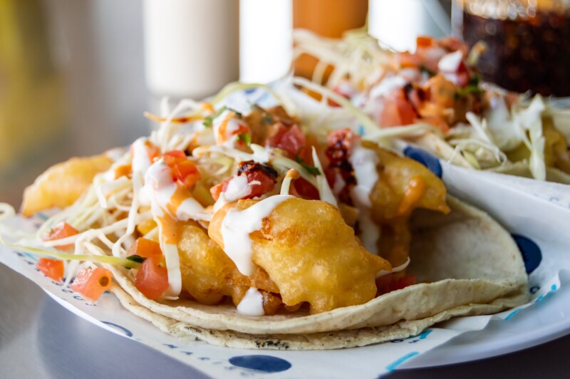 A plate of crispy batter-fried fish tacos, topped with slaw and crema