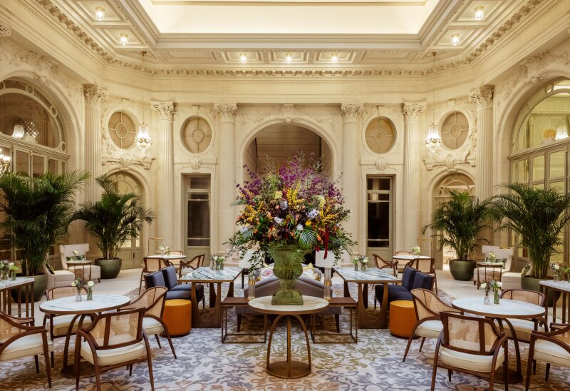 A grand lobby with columns, elegant seating, potted plants, and a large vase of colorful flowers