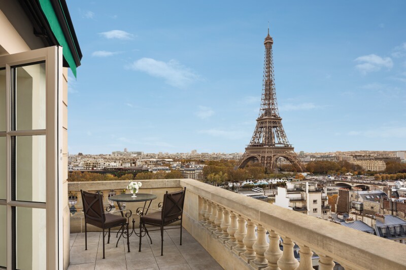 Balcony with two small dark chairs and round table, plus Eiffel Tower in background