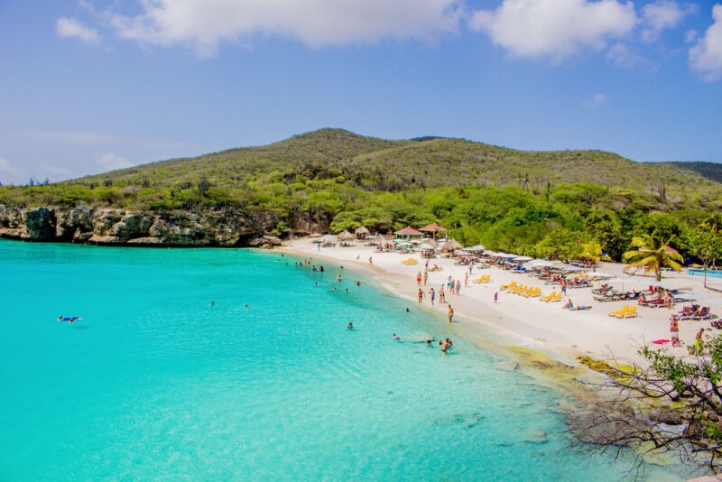 Distant view of people on a beach and in the water, with green hills in background