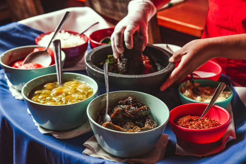 A close-in view of bowls full of ingredients for making salsa with hands working at a mortar and pestle at the Guadalajara Original Grill