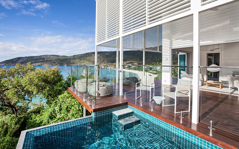 Outdoor deck, with empty white furniture, pool in foreground and beach in background