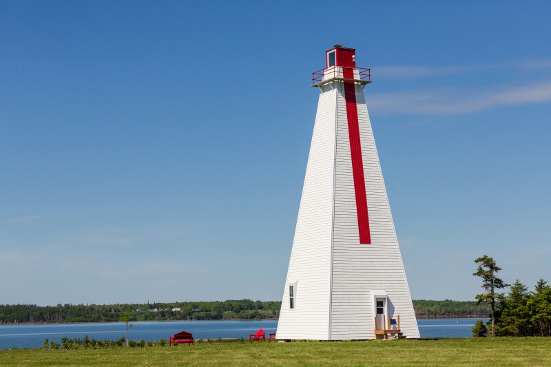 Pyramid-shaped white lighthouse with vertical red stripe on flat shore