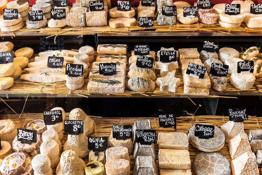 Three rows of different French and Italian cheeses in a small store at the market in the Bastille district