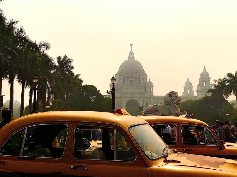 Two vintage-style yellow cabs outside of a historic building in Kolkata, India