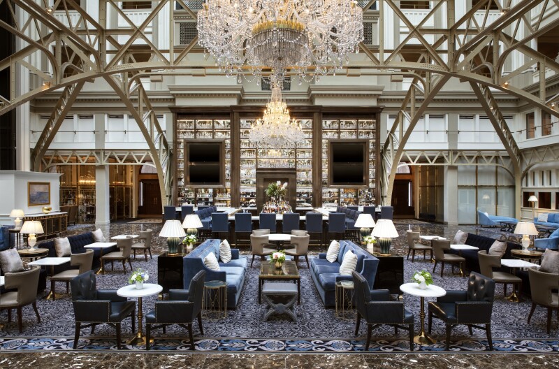 A grand lobby space with skylights, exposed metal supports, crystal chandeliers, and plenty of seating in front of a bar