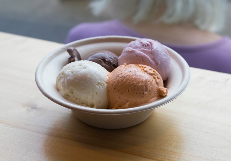 Four scoops of ice cream in white bowl: orange, pink, brown, and white; flavors include Thai tea, chocolate, spruce tips, and fireweed.