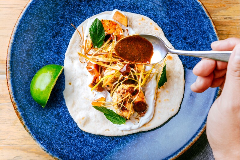 A taco served on a pita, resting on a blue plate with a quarter of a lime next to it