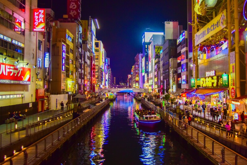 Buildings covered in neon lights at night, with canal running between them