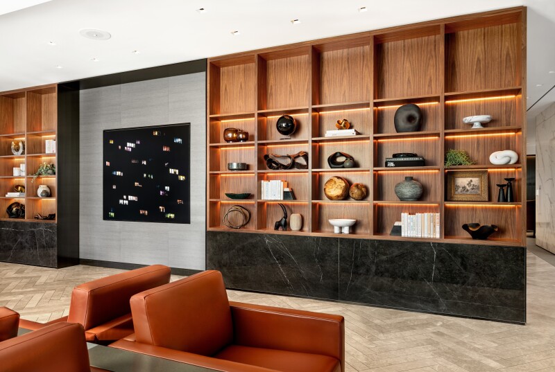 A wooden wall shelving unit displaying art and various objects in the United Polaris Lounge at Chicago O'Hare airport, with some brown armchairs in the foreground